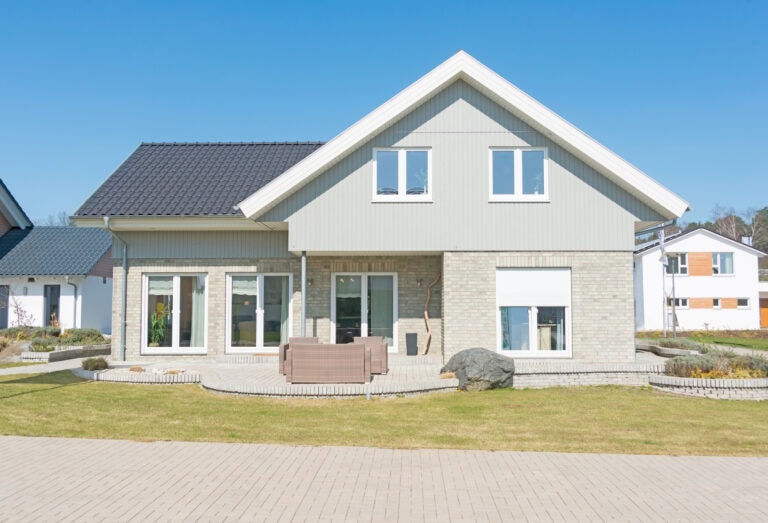 Moderne enebolig med hvit panel og stor hage, beliggende i et rolig nabolag med klare blå himmel og pent opparbeidet uterom.