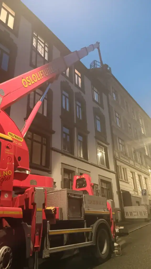 Kran som løfter byggeutstyr i bygatet under kveld, brukt til vedlikehold eller bygging av høy bygning, fokus på sikkerhet og presisjon.